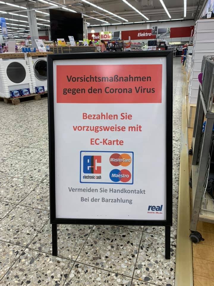 Cartel en una tienda de Alemania que pide tomar precauciones por la crisis del coronavirus y disminuir el contacto en favor de pagar con tarjeta.